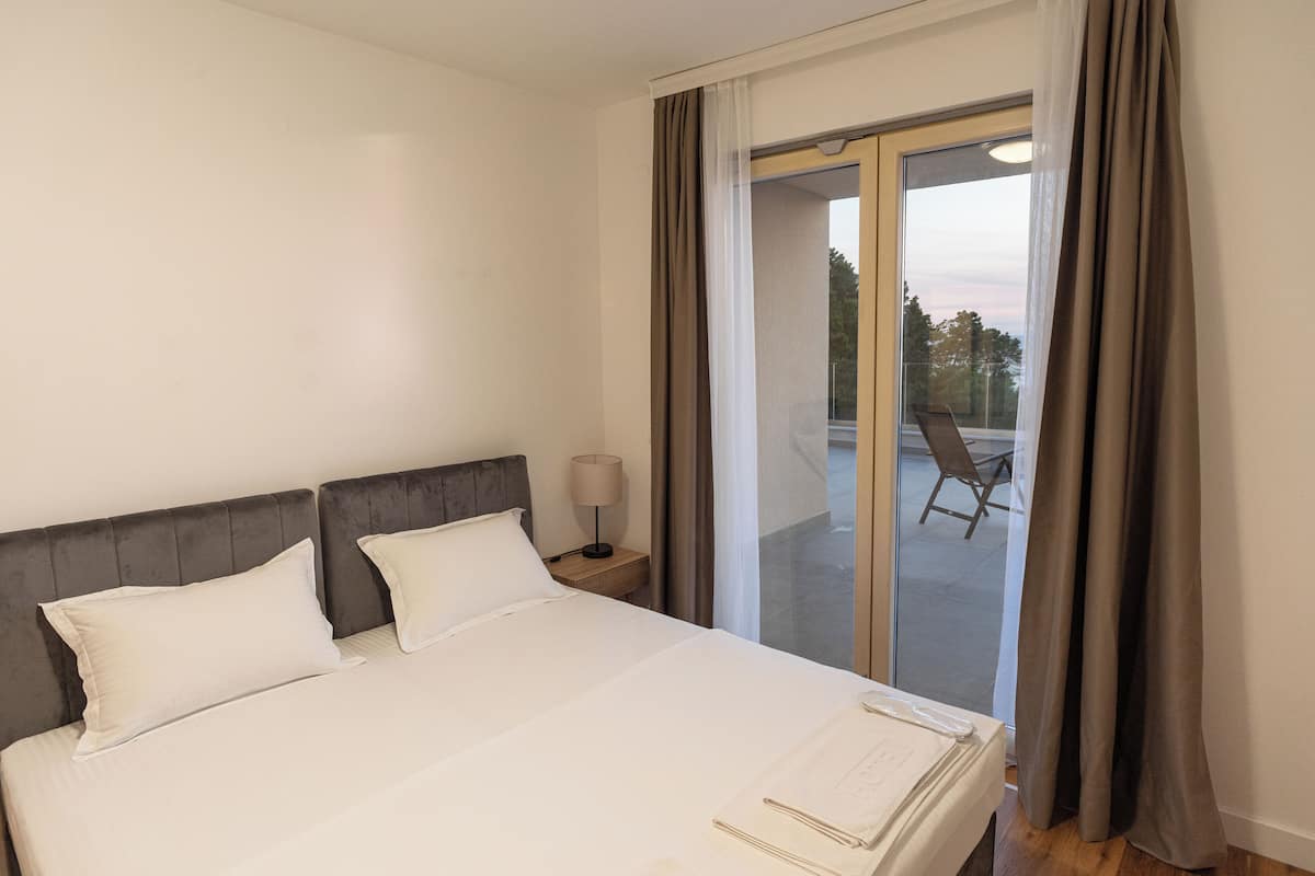 Une chambre d’hôtel avec un grand lit, une table de chevet, une lampe et une vue sur l’extérieur grâce à une porte-fenêtre coulissante.