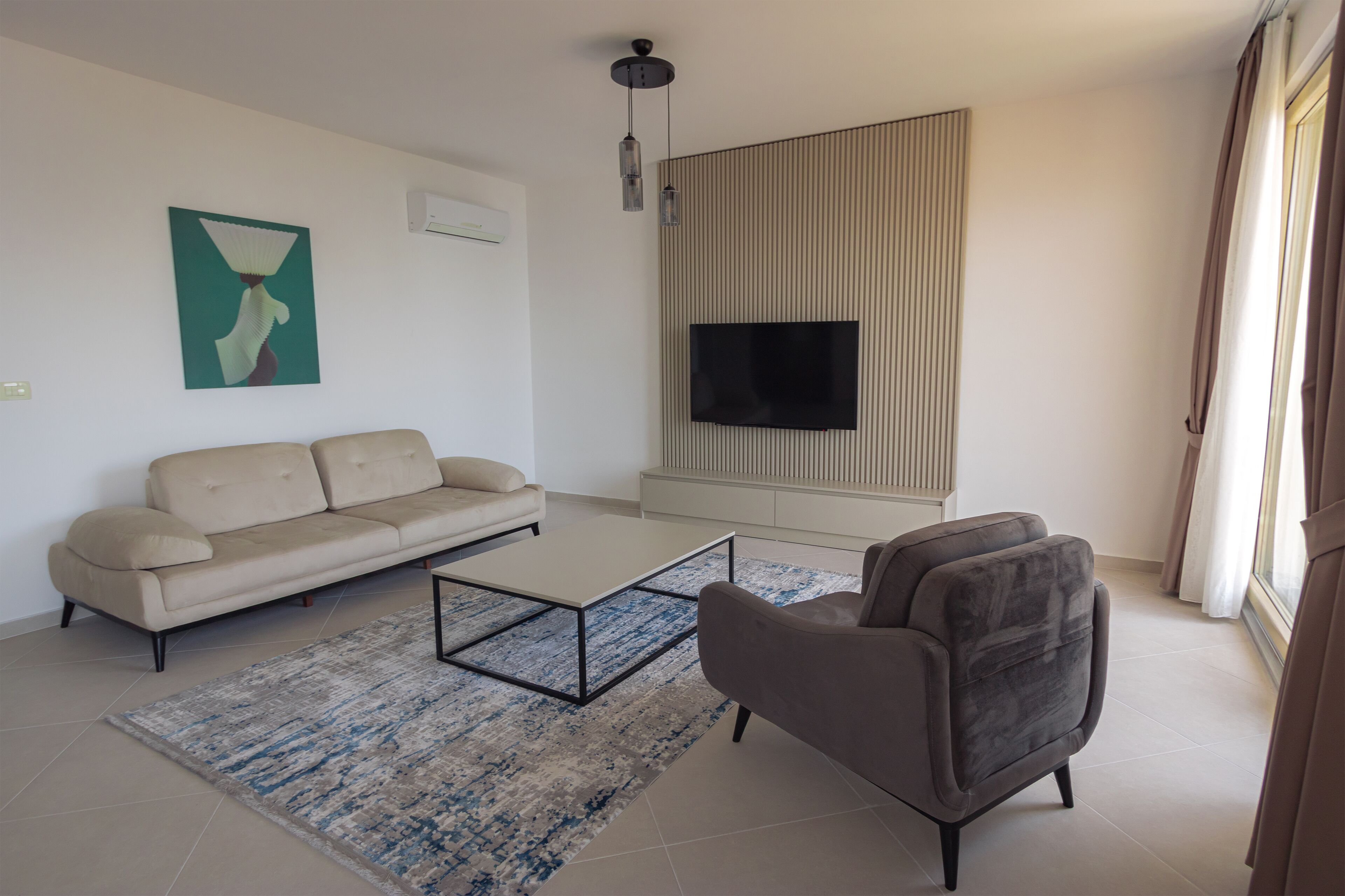 A modern living room with a sofa, a coffee table, a TV on the wall, and a patterned rug.