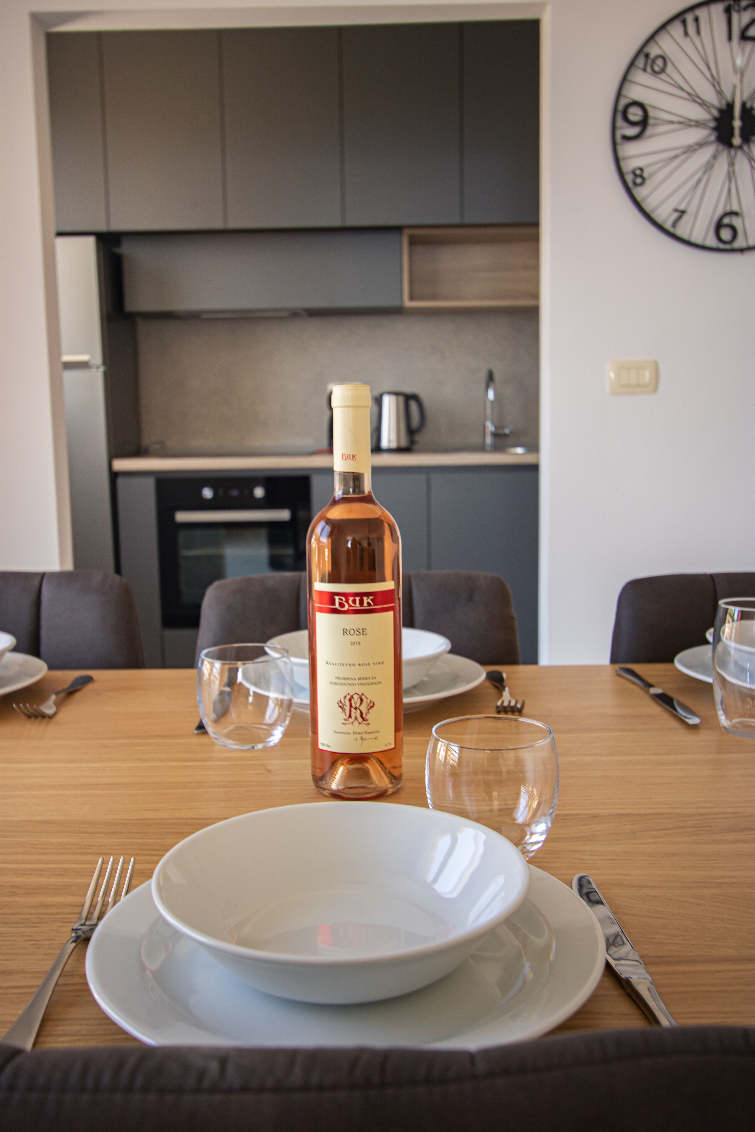 Una mesa de comedor dispuesta con platos, cubiertos y una botella de vino rosado.
