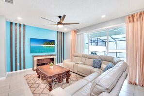 Uma sala de estar moderna com um sofá bege, uma mesa de centro de madeira e uma TV fixada na parede.