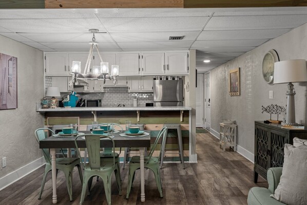 A kitchen with white cabinets, a stainless steel refrigerator, and a dining area with a table and chairs.