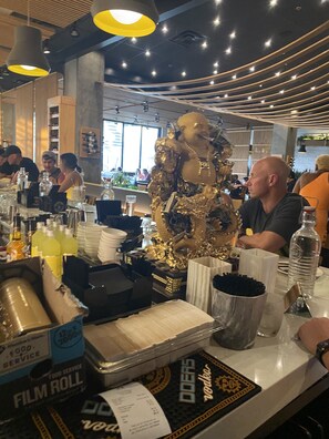 Enjoy a selection of beverages and dining options at this stylish restaurant, featuring a striking golden statue and unique lighting fixtures.