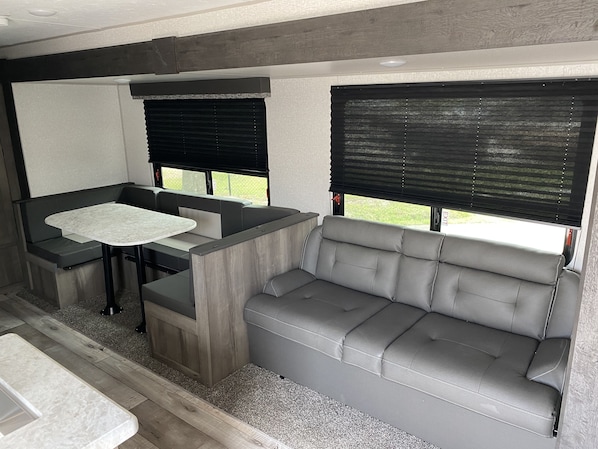 Relax in a compact, modern space with a functional layout, featuring a sofa, dining table, and window with roller blind.
