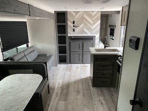 Compact RV interior with a functional layout, featuring a seating area, kitchenette, and storage.