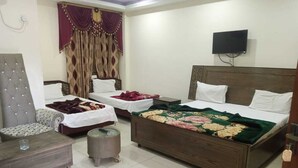 A bedroom with two single beds, a sofa, a chair, a TV, and a small table. - Hotel Continental (Rawalpindi)