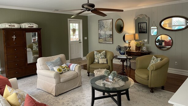 Un salon avec un canapé beige, deux fauteuils, une table basse, un meuble en bois, un ventilateur de plafond et une porte avec une fenêtre.