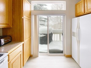 Eine Küche mit Holzausstattung, einem weißen Kühlschrank und einer Glastür zum verschneiten Deck.