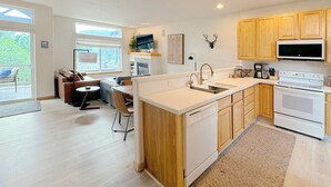 A modern kitchen with wooden cabinets, a built-in dishwasher, a microwave, and a stove. There is a dining area with a table and chairs. - Riverside mountain getaway, million dollar views, ground access, attached garage (Silverthorne)