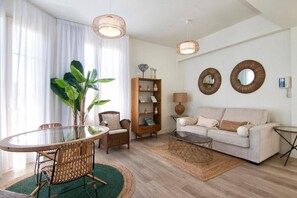 A living room with a round glass table, wicker chairs, a sofa, a bookshelf, and two wall-mounted mirrors. - Alhambra Luxviews Apartment (Granada)