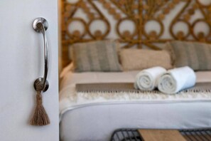 A door with a metallic handle and a tassel, and a bed with rolled towels and a patterned headboard. - Alhambra Luxviews Apartment (Granada)