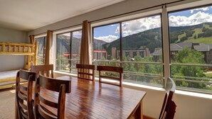 Zona pranzo con tavolo e sedie in legno, ampie finestre con vista sulle montagne.