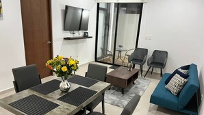A modern living room with a dining table, chairs, a sofa, and a TV mounted on the wall. - New & beautiful apartment (GF) with private pool (Mérida)