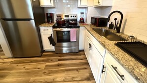 Une cuisine avec des meubles blancs, des appareils en acier inoxydable, un plan de travail en granit et un plancher en bois.