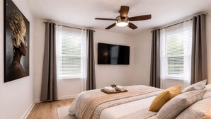 Une chambre à coucher avec un lit, un ventilateur de plafond, un téléviseur à écran plat et un tableau au mur.