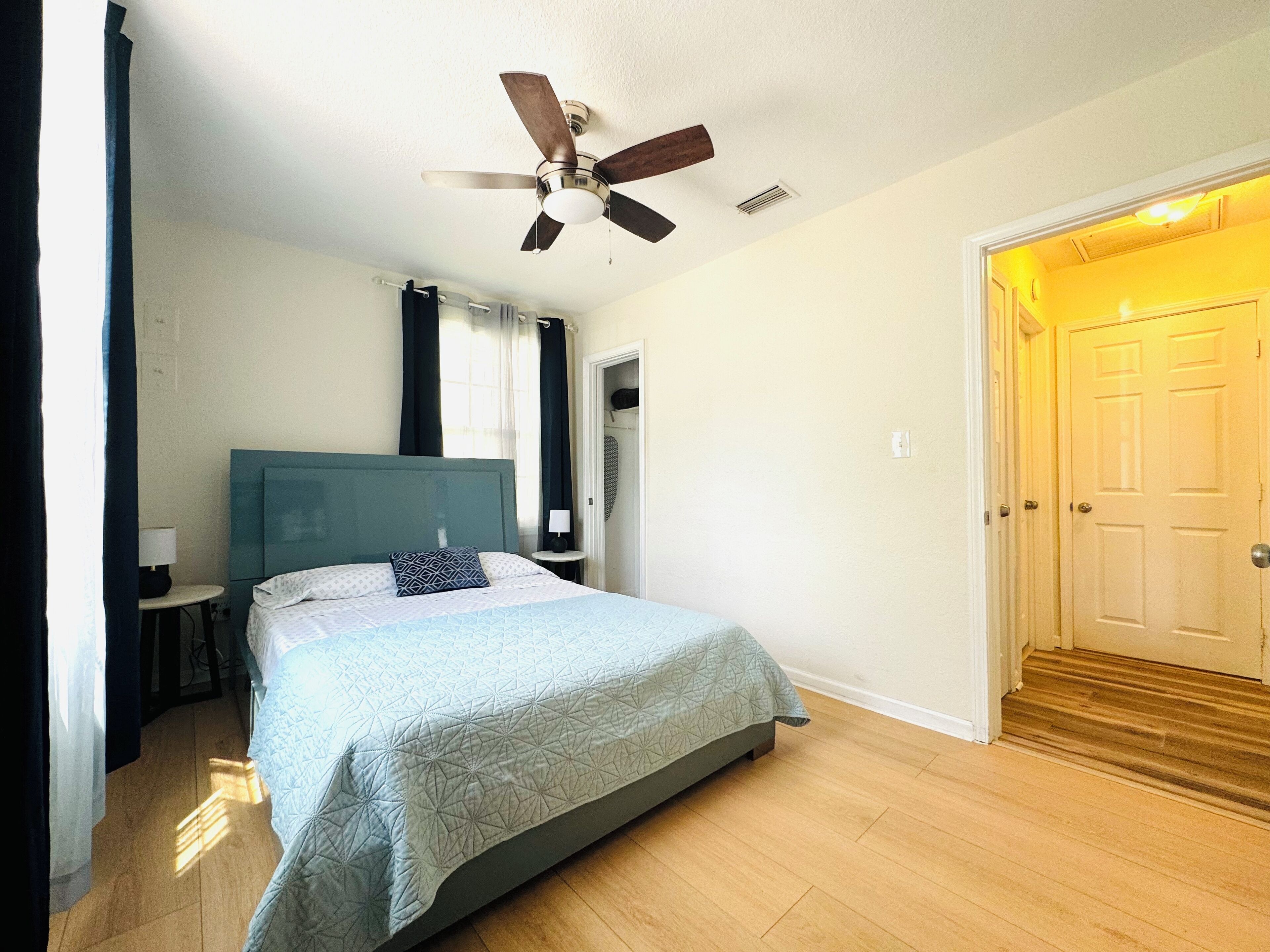A bedroom with a bed, a ceiling fan, a nightstand, a lamp, and a door.