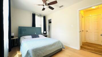 A bedroom with a bed, a ceiling fan, a nightstand, a lamp, and a door.