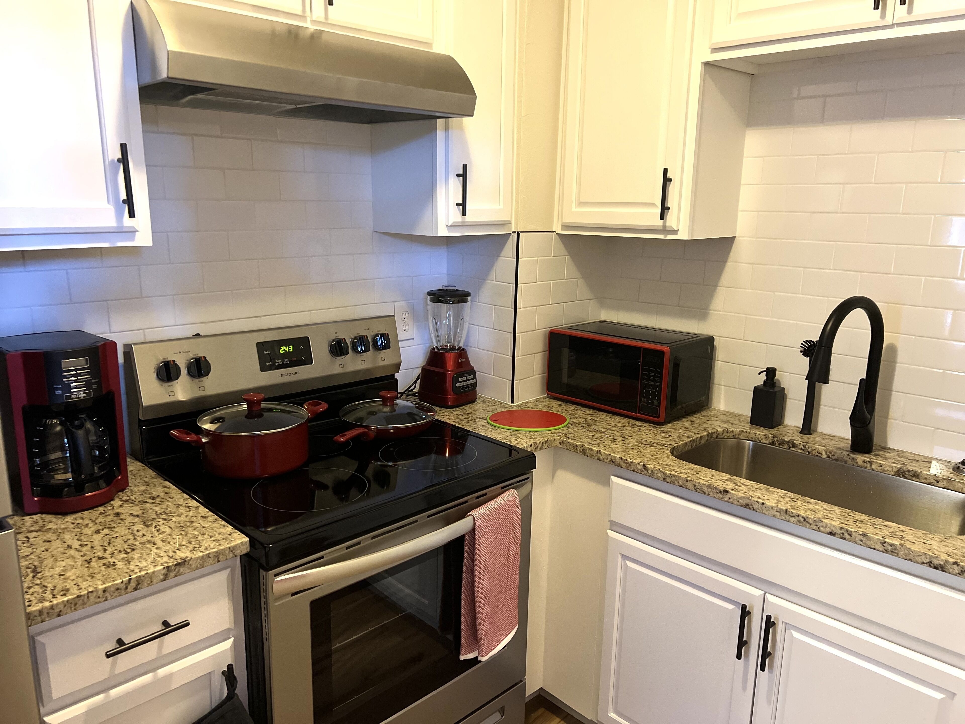 A kitchen with white cabinets, a stove, a microwave, and a coffee maker.