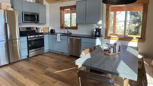 A modern kitchen with light blue cabinets, stainless steel appliances, and a wooden dining table.