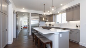 Een moderne keuken met een groot eiland, barkrukken, roestvrijstalen apparatuur en hanglampen.