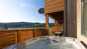 Een hottub op een houten terras, met uitzicht op een bebost landschap.