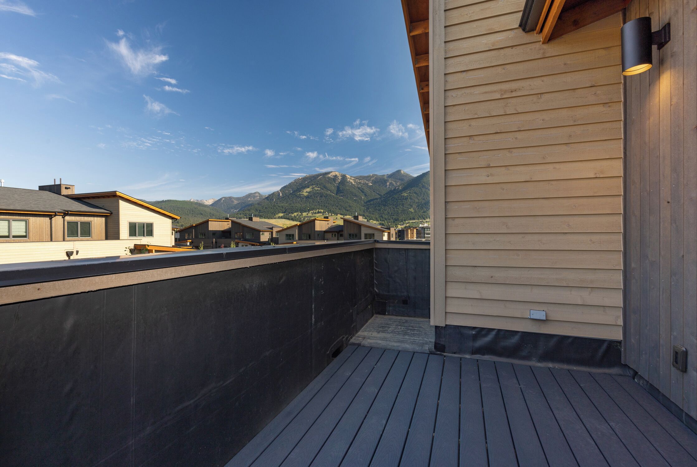 A rooftop terrace with a view of mountains, wooden deck, and a building with a light fixture.