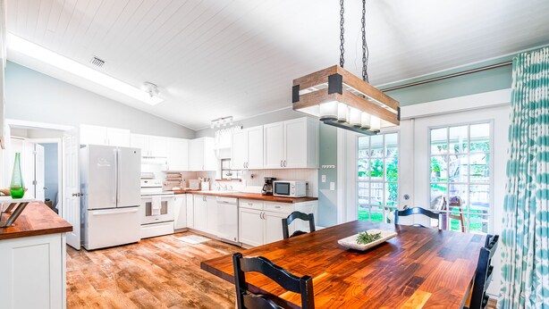 Una cocina moderna con armarios blancos, una mesa de comedor de madera y una lámpara colgante.