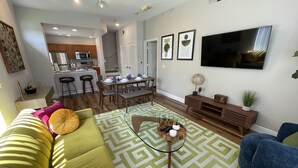 Un salon moderne avec un canapé vert, des fauteuils bleus, une table basse et un téléviseur.