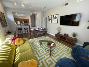 A modern living room with a green sofa, blue chairs, a coffee table, and a TV.