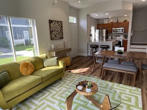 A modern living room with a green sofa, a coffee table, and a dining area with a wooden table and chairs.