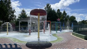 Un espace de jeux aquatiques doté de plusieurs jets d’eau et, en arrière-plan, un kiosque.