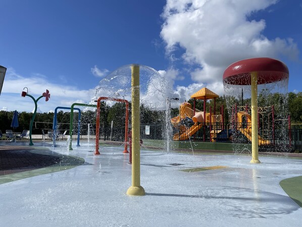 A water play area with multiple water jets and a playground structure in the background.
