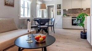 A modern living room with a sofa, a dining table with chairs, a kitchen area with cabinets, and a potted plant.