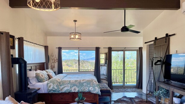 Un dormitorio amplio con una cama grande, ventilador de techo, televisor y vistas al exterior.