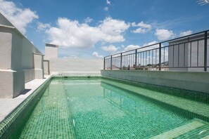 Une piscine située sur le toit, avec une eau d’un bleu limpide, entourée d’un bâtiment blanc et d’une rambarde en métal.