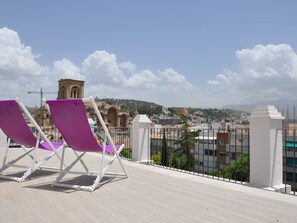 A rooftop terrace with two purple lounge chairs and a view of a historic building in the distance.