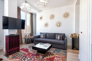Een woonkamer met een grijze bank, een bijzettafeltje, een flatscreen televisie, een rode kast en decoratieve spiegelwanden.
