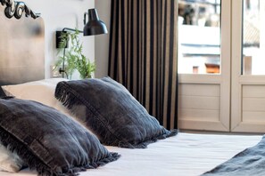 Een bed met donkere, geribbelde kussens, een zwarte bureaulamp en een plant op een nachtkastje.