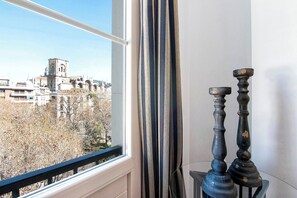 A window with a view of a cityscape, including a church tower, and a pair of dark, ornate candle holders.