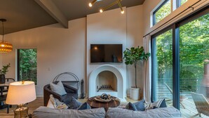 Ein modernes Wohnzimmer mit Kamin, einer Sofagarnitur, einem Esstisch und großen Fenstern mit Blick ins Freie.
