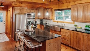 A spacious kitchen with wooden cabinets, a large island with bar stools, stainless steel appliances, and pendant lighting. - Boutique All Wood Cottage in the Woods (Lanark)