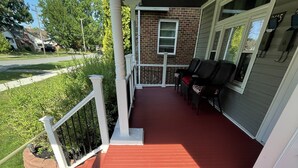 A covered outdoor area with a red floor, white railings, and a brick wall. - Downstairs Unit near National Park + Downtown Cleveland (Cleveland)