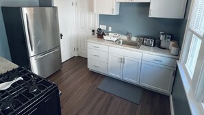 A modern kitchen with white cabinets, a stainless steel refrigerator, a gas stove, and a ceiling fan. - Downstairs Unit near National Park + Downtown Cleveland (Cleveland)