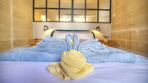 Ein Hotelzimmer mit Bett, zwei Nachttischen, einem Fenster mit Jalousien und Handtüchern, die zu einem Schwan geformt sind.