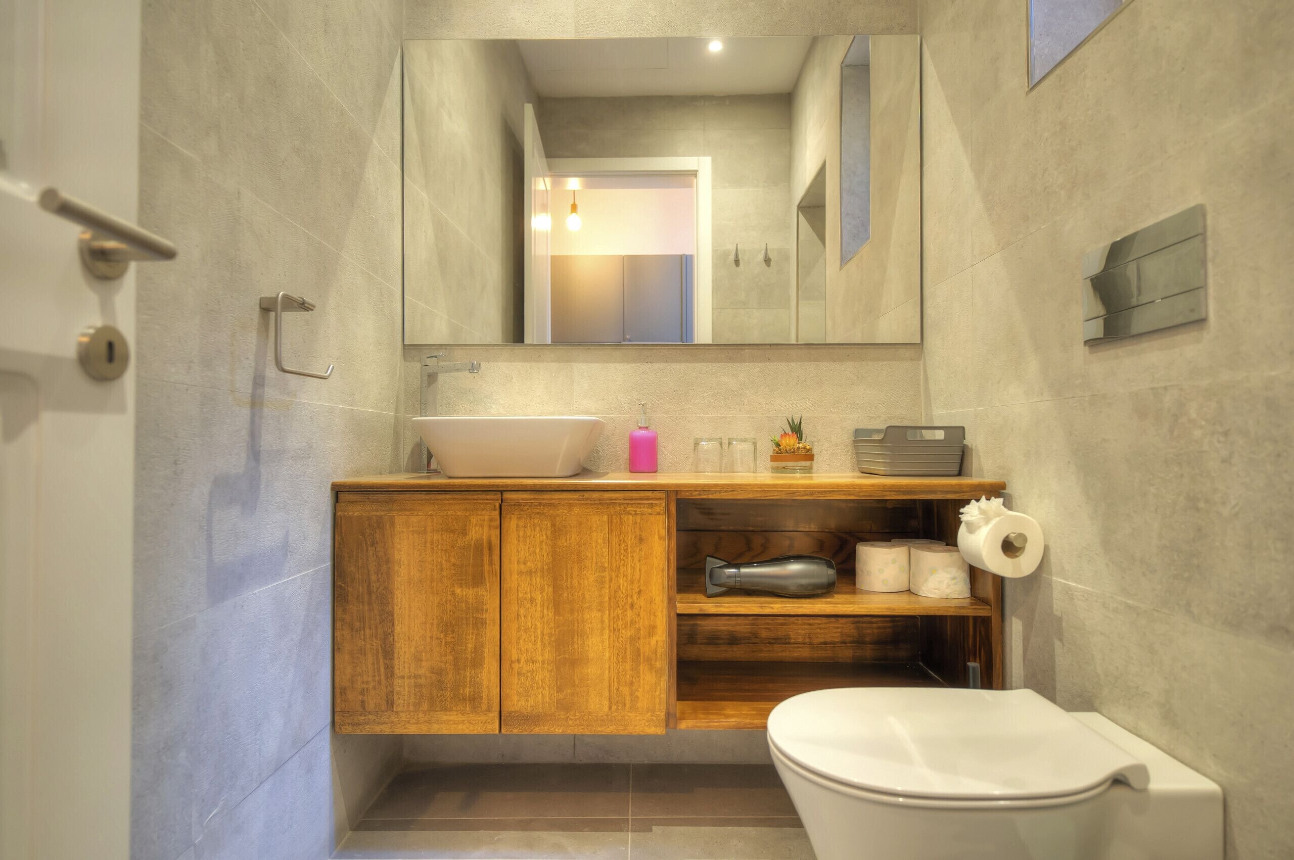 Ein modernes Badezimmer mit einem Holzwaschtisch, einem großen Spiegel, einem Waschbecken und einer Toilette.