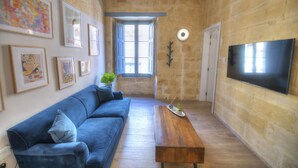 Ein Wohnzimmer mit einem blauen Sofa, einem Holztisch und einem an der Wand befestigten Fernseher.