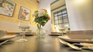Ein Esstisch ist gedeckt mit Tellern, Schüsseln und Weingläsern, in der Mitte steht eine Blumenvase.