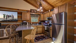A wooden cabin kitchen with a large island, stainless steel appliances, and a television mounted above the island. - Romantic and Cozy! 2 Bed 2 Bath True Log Cabin close to Park and Attractions!  (Gatlinburg)