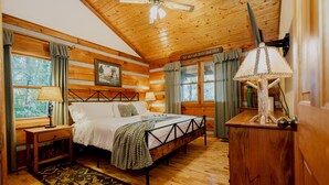 A log cabin bedroom with a bed, wooden floors, a ceiling fan, and a rustic decor style. - Romantic and Cozy! 2 Bed 2 Bath True Log Cabin close to Park and Attractions!  (Gatlinburg)