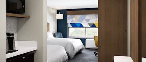 Une chambre d’hôtel moderne équipée d’un lit, d’un bureau, d’une chaise, d’une télévision et d’une fenêtre agrémentée d’un rideau à motifs géométriques.
