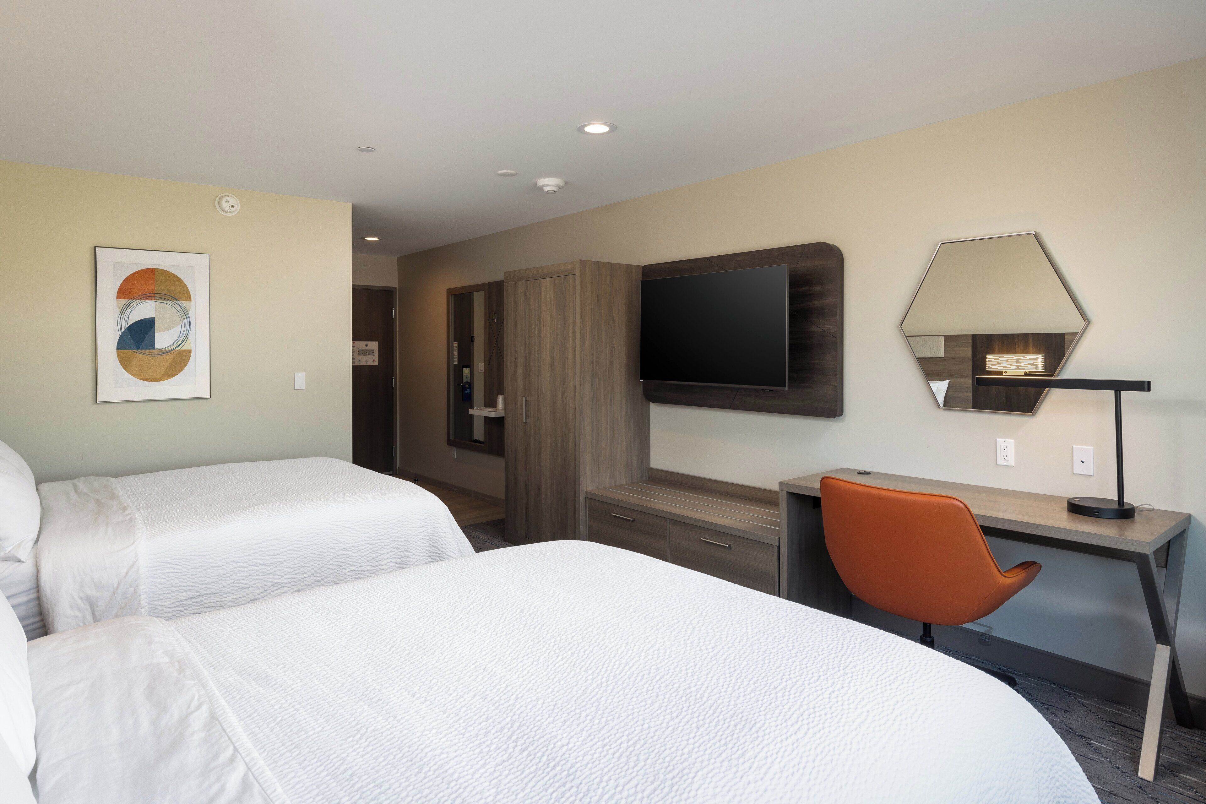 A hotel room with two beds, a desk, a chair, a TV, and a mirror.